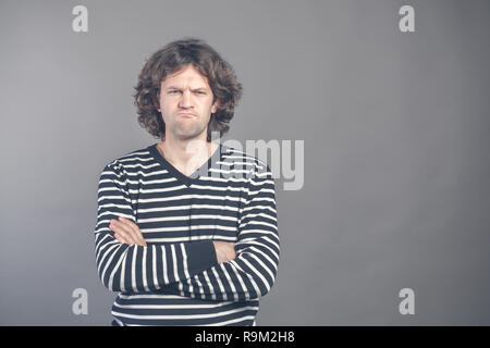 Closeup Portrait von zornig, wütend, grantige Mann im gestreiften Pullover schlechte Haltung, die Arme verschränkt, gefaltet, in der Sie suchen, isoliert, grauen Hintergrund. Neg Stockfoto