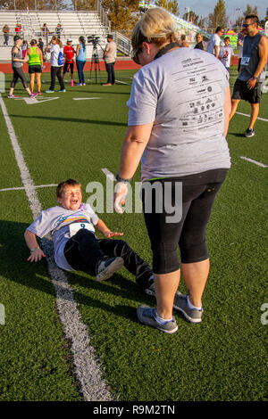 Als seine Mutter verbindlich seine Zehen hält, ein 8-jähriger Junge hat einige vorbereitende Sit Ups vor der Ausführung in einer Gemeinschaft Wettlauf im Costa Mesa, CA. Stockfoto