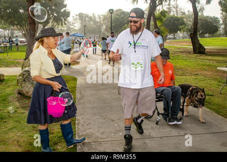 Marchers in einem fundraising Charity Event für Behinderte Blasen der Ermutigung von einem gut wisher auf einem Park Weg in Costa Mesa, CA. Hinweis Teilnehmer im Rollstuhl. Stockfoto