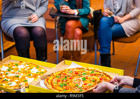 Verschiedene leckere und heiße Pizza Slices auf einer Tabelle zwischen sitzen alle Menschen Stockfoto
