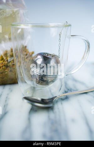 Innerhalb der Kaffee Glas Schale haben wir einen Tee Ball. Wir sehen auch eine transparente Tasche mit getrocknete Kamillenblüten. Stockfoto