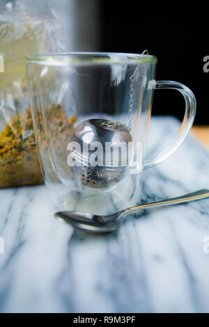 Innerhalb der Kaffee Glas Schale haben wir einen Tee Ball. Wir sehen auch eine transparente Tasche mit getrocknete Kamillenblüten. Stockfoto