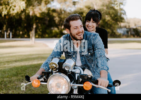 Portrait von attraktiven gut aussehende junge moderne Trendy modische Kerl Mädchen Paar Reiten auf Grün Motorrad Cruiser Classic Bike in der Liebe Stockfoto