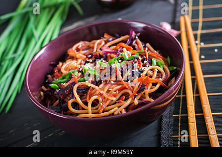 Chinesisches Essen. Vegan fry Nudeln mit Rotkohl und Karotten in einer Schüssel verrühren auf schwarzem Holz- Hintergrund. Asiatische Küche essen. Stockfoto