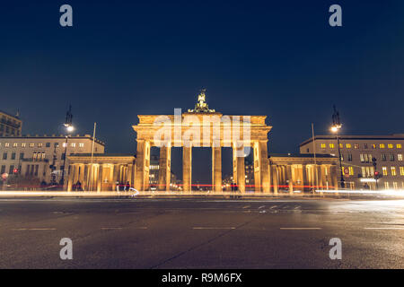 Brandenburger Tor in Berlin bei Nacht mit Sicht nach hinten. Laternen die Straße ausleuchten. Licht aus vorbeifahrenden Autos sichtbar ist. Das Denkmal ist beleuchtet Stockfoto