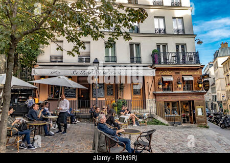 Leute, die sich an Tischen vor dem Restaurant Le Relais de la butte entspannen, während ein Kellner eine Bestellung eines Kunden in Montmartre, Paris, annimmt Stockfoto