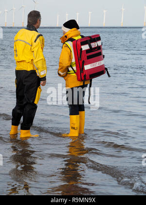 Redcar Cleveland England 26. Dezember 2018. Die jährlichen Boxing Day Liebe 'ip' wurde heute in ungewöhnlich mildes Wetter mit Massen von Menschen an und mit der Rnli und Küstenwache schauen für Sicherheit am Strand in Redcar während, wenn Leute in Fancy Dress gehen in die Nordsee für Spaß und Geld für ihre Nächstenliebe zu heben. Hier zwei rettungsbootleute stehen im flachen Wasser, einer trägt einen Erste Hilfe Rucksack Credit: Peter Jordan NE/Alamy leben Nachrichten Stockfoto