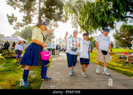 Marchers in einem fundraising Charity Event für Behinderte Blasen der Ermutigung von einem gut wisher auf einem Park Weg in Costa Mesa, CA. Hinweis Teilnehmer im Rollstuhl. Stockfoto