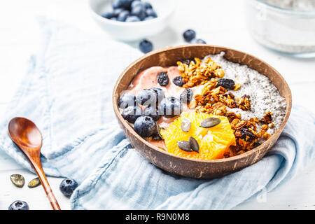 Vegan smoothie Schüssel mit Chia Pudding, Beeren und Müsli in einem coconut Shell auf einem weißen Holz- Hintergrund. Auf Basis pflanzlicher Ernährung Konzept. Stockfoto