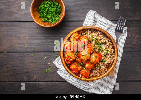 Huhn Hackfleischbällchen in Tomatensauce mit Buchweizen in eine hölzerne Schüssel auf einem dunklen Hintergrund. Stockfoto