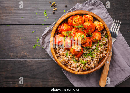 Huhn Hackfleischbällchen in Tomatensauce mit Buchweizen in eine hölzerne Schüssel auf einem dunklen Hintergrund. Stockfoto