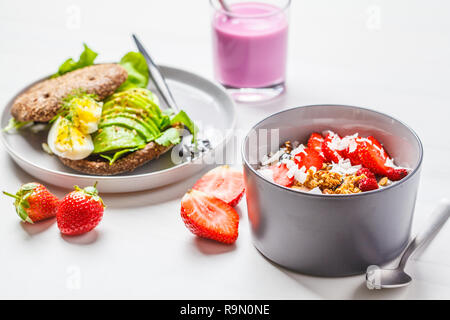 Strawberry smoothie Schüssel mit Müsli, Kokos, Beeren und Avocado Toast auf einem weißen Hintergrund. Gesunde vegane Ernährung Konzept. Stockfoto