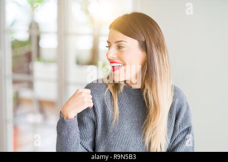 Junge schöne Frau winter Pullover zu Hause weg schauen mit einem Lächeln auf dem Gesicht zu Seite, natürlicher Ausdruck. Lachend zuversichtlich. Stockfoto