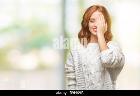 Junge schöne Frau über isolierte Hintergrund tragen Winter pullover Abdecken eines Auges mit der Hand mit selbstbewussten Lächeln auf dem Gesicht und Überraschung Emotion. Stockfoto