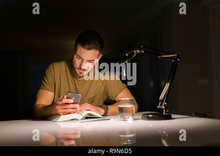 Jungen gutaussehenden Mann zu Hause studieren, mit Smartphone, am Telefon suchen Stockfoto