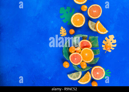 Exotische Früchte flach. Mango, Orangen, kumquat und andere tropische Früchte auf einer monstera Platte. Hellen blauen Hintergrund mit kopieren. Stockfoto