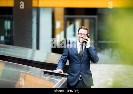 Lächelnd Geschäftsmann Smartphone sprechen in der Nähe des Bürogebäudes Stockfoto