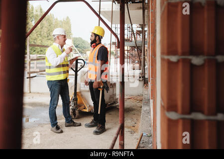 Menschen, die in Baustelle. Männer bei der Arbeit im neuen Haus im Haus. Teamwork mit Foreman erteilen Anweisungen an die Arbeitnehmer wi Handbuch Stockfoto
