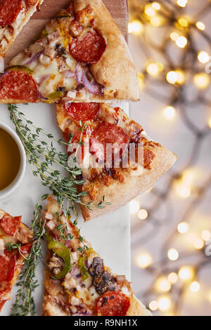 Weihnachten und Neujahr Atmosphäre. Heiße italienische Pizza mit Schmelzen mit Tomate, Salami und Käse auf einem weißen Marmor Schneidebrett. Hintergrund mit Beleuchtung Stockfoto