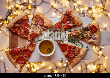 Weihnachten und Neujahr Atmosphäre. Heiße italienische Pizza mit Schmelzen mit Tomate, Salami und Käse auf einem weißen Marmor Schneidebrett. Hintergrund mit Beleuchtung Stockfoto
