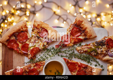 Weihnachten und Neujahr Atmosphäre. Heiße italienische Pizza mit Schmelzen mit Tomate, Salami und Käse auf einem weißen Marmor Schneidebrett. Hintergrund mit Beleuchtung Stockfoto