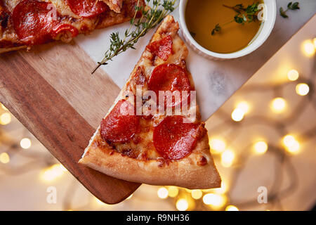 Weihnachten und Neujahr Atmosphäre. Heiße italienische Pizza mit Schmelzen mit Tomate, Salami und Käse auf einem weißen Marmor Schneidebrett. Hintergrund mit Beleuchtung Stockfoto