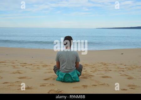 Mann sitzt im Schneidersitz, Meer Genießen, Entspannen und Nachdenken über die Welt. Stockfoto