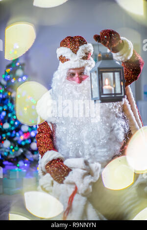 Santa bringt Geschenke. Santa Claus mit einer Kerze Laterne ist auf der Suche nach Geschenke im Sack. Stockfoto