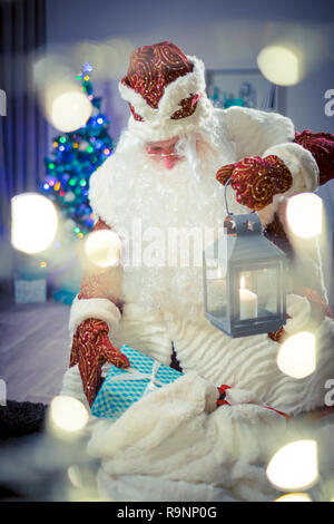 Santa bringt Geschenke. Santa Claus mit einer Kerze Laterne ist auf der Suche nach Geschenke im Sack. Stockfoto