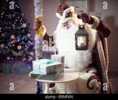 Santa bringt Geschenke. Santa Claus mit einer Kerze Laterne ist auf der Suche nach Geschenke im Sack. Stockfoto