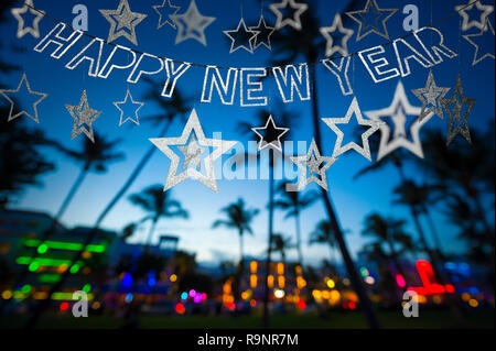Frohes Neues Jahr Nachricht hängen in glitzerndem Partei Bunting über tropischen Palmen des glühenden Neon Lichter der Skyline von Miami Beach, Florida, Stockfoto