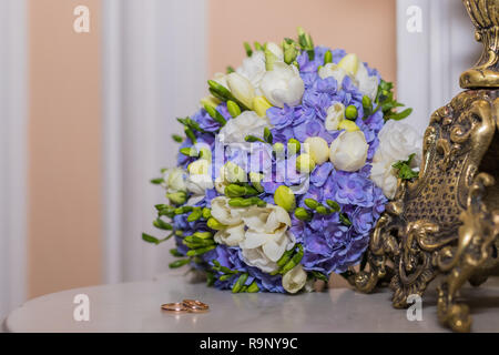 Trauringe liegen und Schönen Blumenstrauß als brautzusätze. zwei goldene Ringe und Hochzeit Blumen. Grußkarte, Einladung, bunte Blumen weiße und blaue Freesie und Hortensien. Platz kopieren Stockfoto