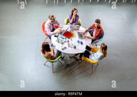 Team von einem jungen Mitarbeiter lässig gekleidet gemeinsam mit Laptops am runden Tisch sitzen im Büro, Ansicht von oben Stockfoto