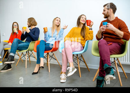 Jungen Mitarbeiter sitzen auf dem bunten Stühlen während der Kaffeepause auf der weißen Wand Hintergrund Stockfoto