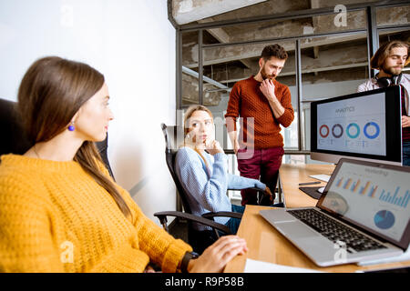 Gruppe von jungen Mitarbeiter gekleidet beiläufig zusammen auf dem Computer mit einigen Diagrammen sitzt im modernen Büro innen Stockfoto