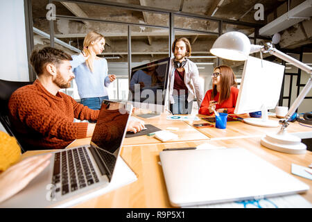Gruppe von jungen Mitarbeiter gekleidet beiläufig zusammen auf dem Computer in das moderne Büro innen Stockfoto
