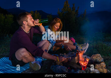 Mann und Frau rosting Würstchen am Lagerfeuer, trinken Bier und ...