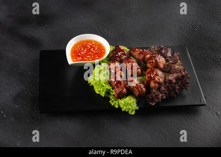 Schweine in Decken. Kleine Würstchen eingewickelt in geräucherten Speck in Auflaufform Stockfoto