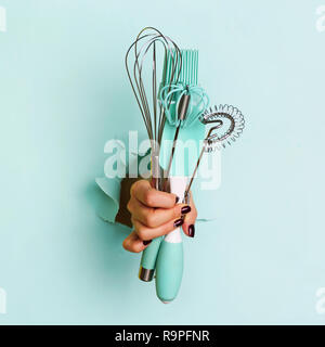 Frau hand Küchengeräte auf blauem Hintergrund. Backen Werkzeuge Pinsel, Schneebesen, teigschaber. Bäckerei, Kochen, gesunde Hausmannskost Konzept. Kopieren spa Stockfoto