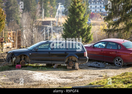 Rotes Auto in Freizeit und alten rostigen gebrochen Papierkorb Auto nach einem Crash Unfall ohne Räder auf Holz Stempel an einem sonnigen Tag im Freien auf Abgebrochen Stockfoto