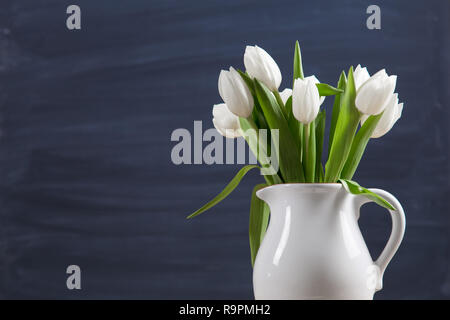 Blumenstrauß aus den weißen Tulpen in einem altmodisch Rustikal vase Topf. Helle Farbe Blumen in Weiß Kanne auf schiefertafel Hintergrund. Stockfoto
