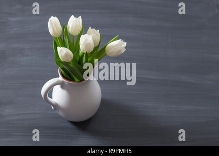 Blumenstrauß aus den weißen Tulpen in einem altmodisch Rustikal vase Topf. Helle Farbe Blumen in Weiß Kanne auf schiefertafel Hintergrund. Stockfoto