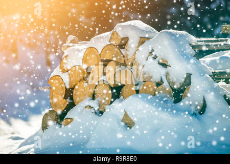 Fein säuberlich gestapelt Stapel von gehackten trocken Trunks Holz mit Schnee im Freien auf hellen, kalten Winter sonniger Tag fallen, große Schneeflocken Abstract Background, Feuer Woo Stockfoto