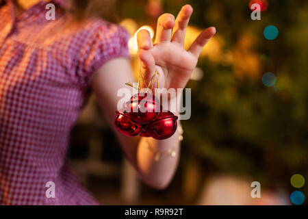 Drei kleine rote Jingle bells in der Hand des Kindes. Stockfoto