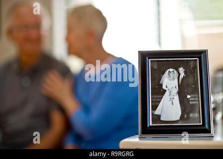 Gerne älteres Paar hinter ein gerahmtes Foto von einem jungen Paar, das am Tag ihrer Hochzeit sitzen. Stockfoto