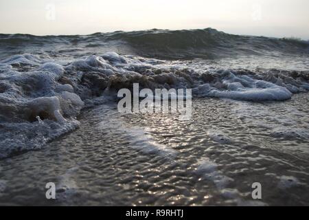 Kleine Wellen ein Strand wie die Ebbe geht, Curling, den Sand und die schmutzige Blasen mit sauberen, weißen Schaum gemischt, wie größere Wellen bauen in der b Stockfoto