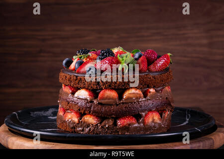 Schokoladenkuchen mit frischen Erdbeeren und Früchte auf Holz- Hintergrund. Stockfoto