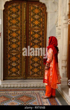 Indische Frau trägt einen schönen orange Sari steht vor einem reich verzierten bemalte hölzerne Tür Junagarh Fort Bikaner Rajasthan Indien Stockfoto