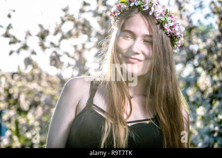 Schönen Lächeln unschuldig reine Mädchen in einem Kranz mit Blumen der weißen Apple Blossom, Feder outdoor portrait von frau Gesicht mit den Armen Stockfoto