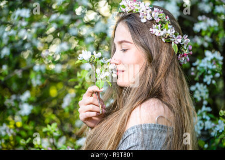 Schöne junge Frau im Frühling Garten unter einem blühenden Bäumen und Apple blumen Kranz auf dem Kopf. Natürliche schöne Mädchen duftende Blüten im Obstgarten. Stockfoto